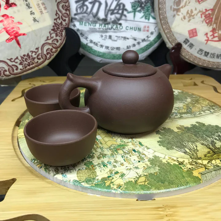Purple clay teapot with two matching cups on a painted round tray