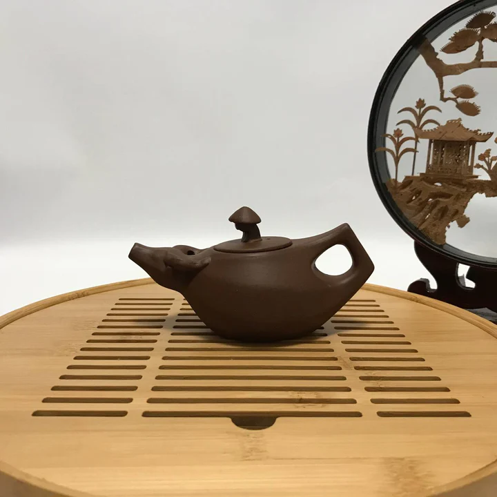 Low boat-shaped clay teapot on a bamboo draining tray
