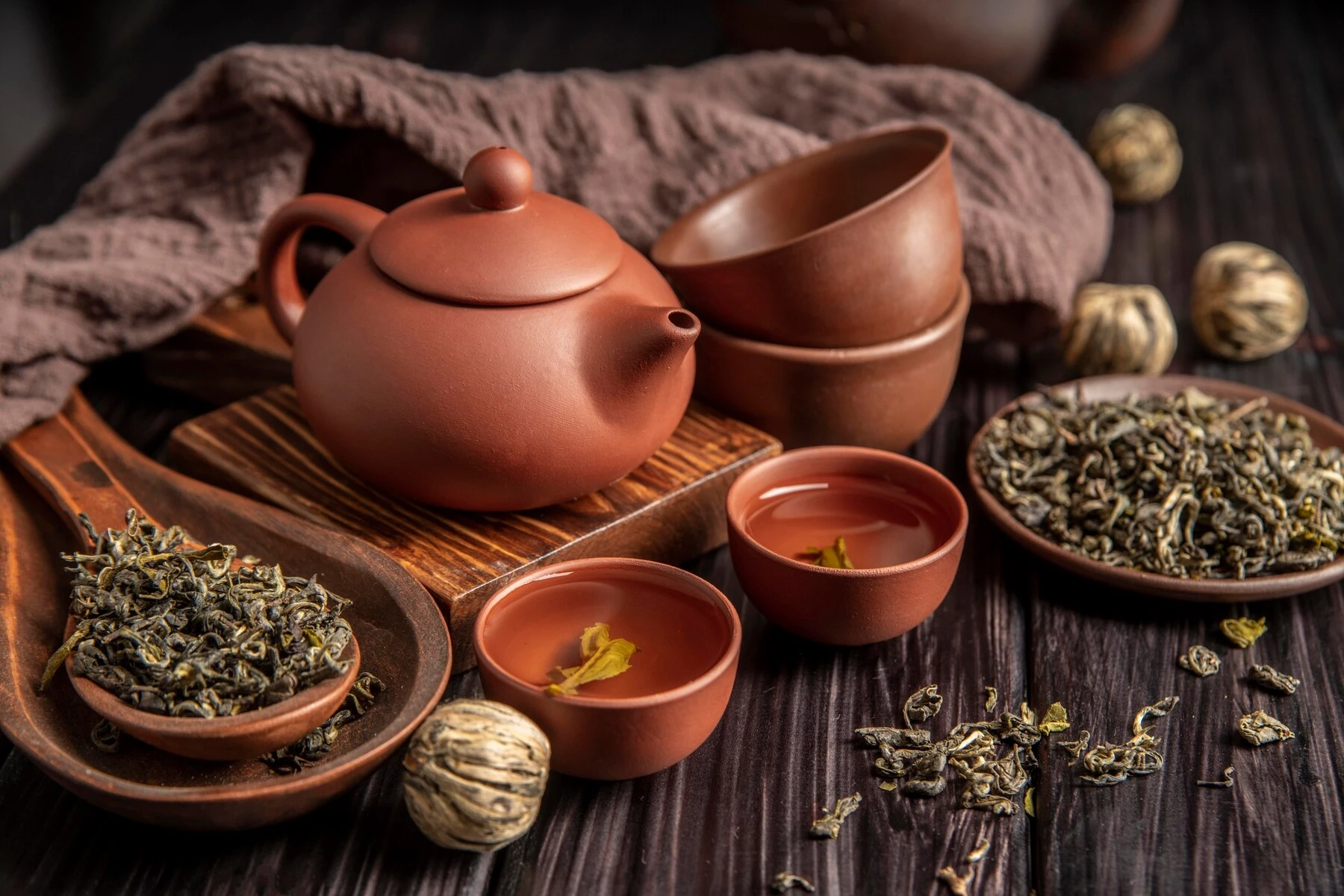 A clay teapot and a glass of amber tea resting on a bamboo tray